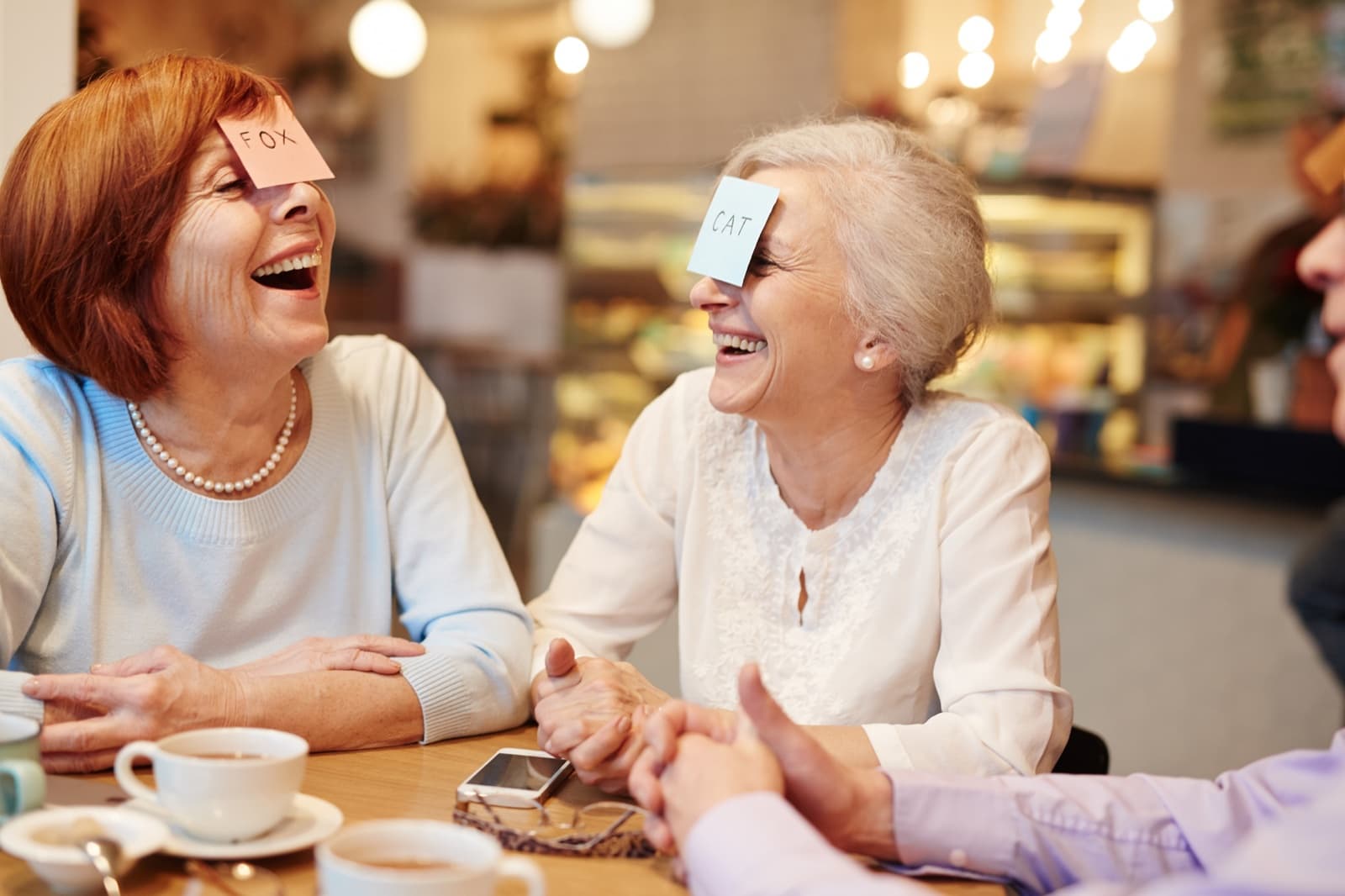 Two friends laughing together while playing a guessing game at a café table