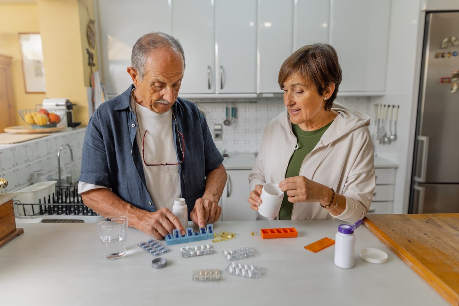 Caregiver helping an older adult organize daily medications at a kitchen counter