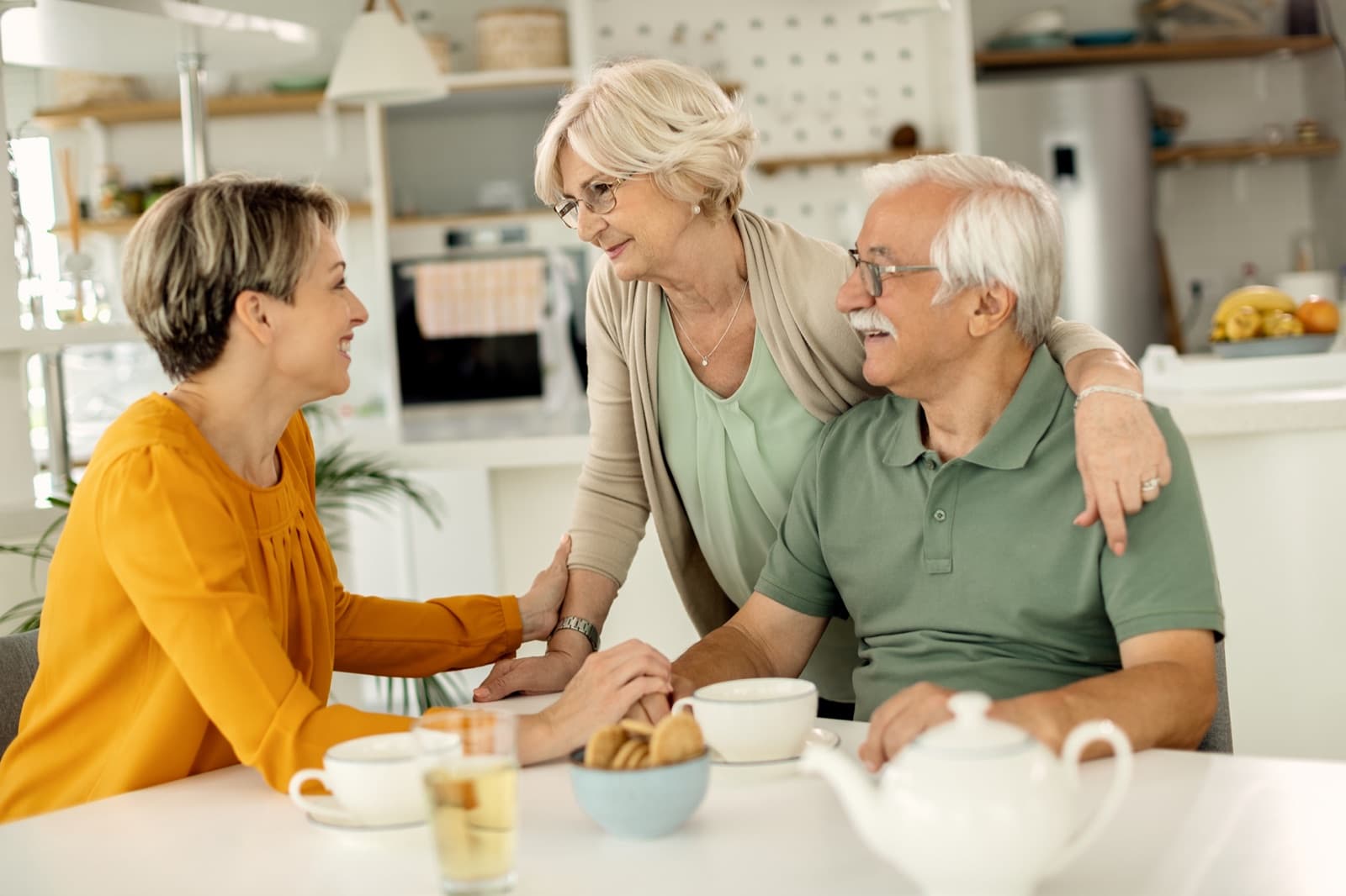 Caregiver sharing tea with an older couple at a kitchen table