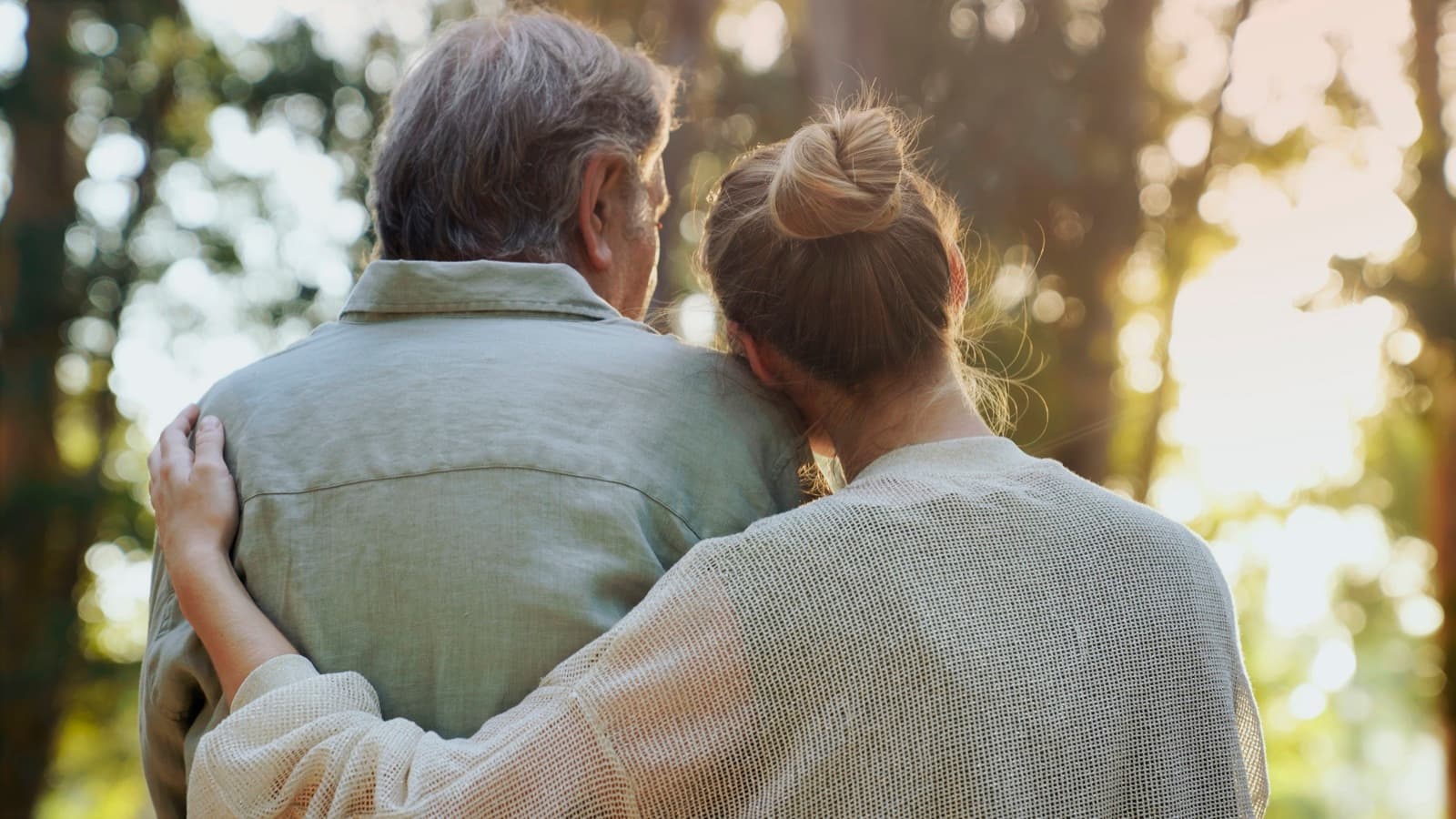 Adult daughter resting her head on her father's shoulder during a peaceful walk outdoors together